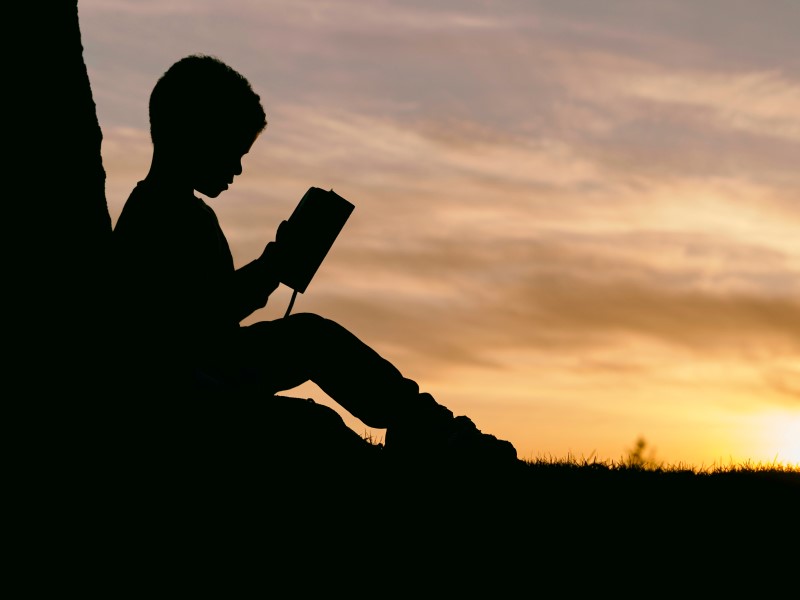 silhouette of boy reading a book outside