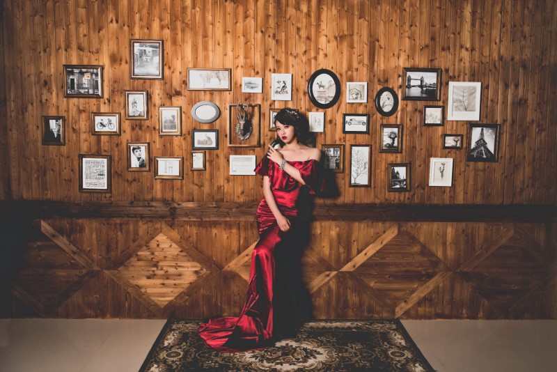 woman in red dress in front of framed photographs hanging on wood paneled wall