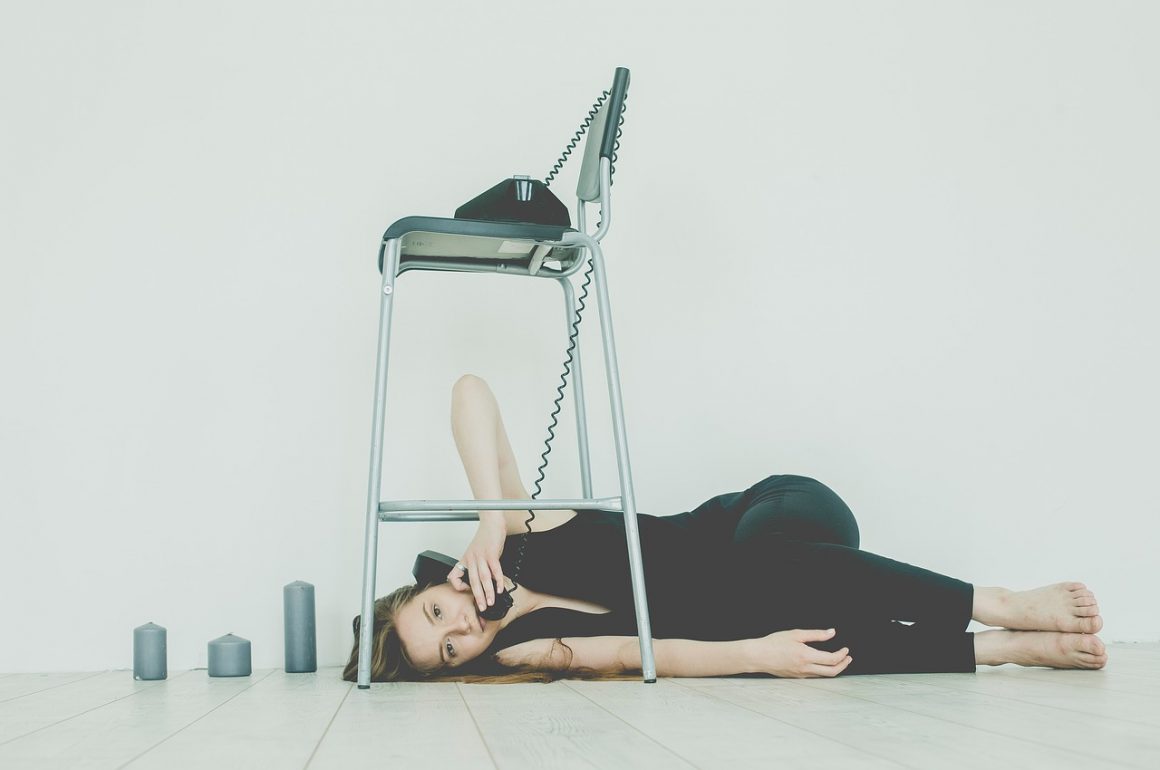 woman lying on the ground under a chair talking on an old-fashioned phone with a cord