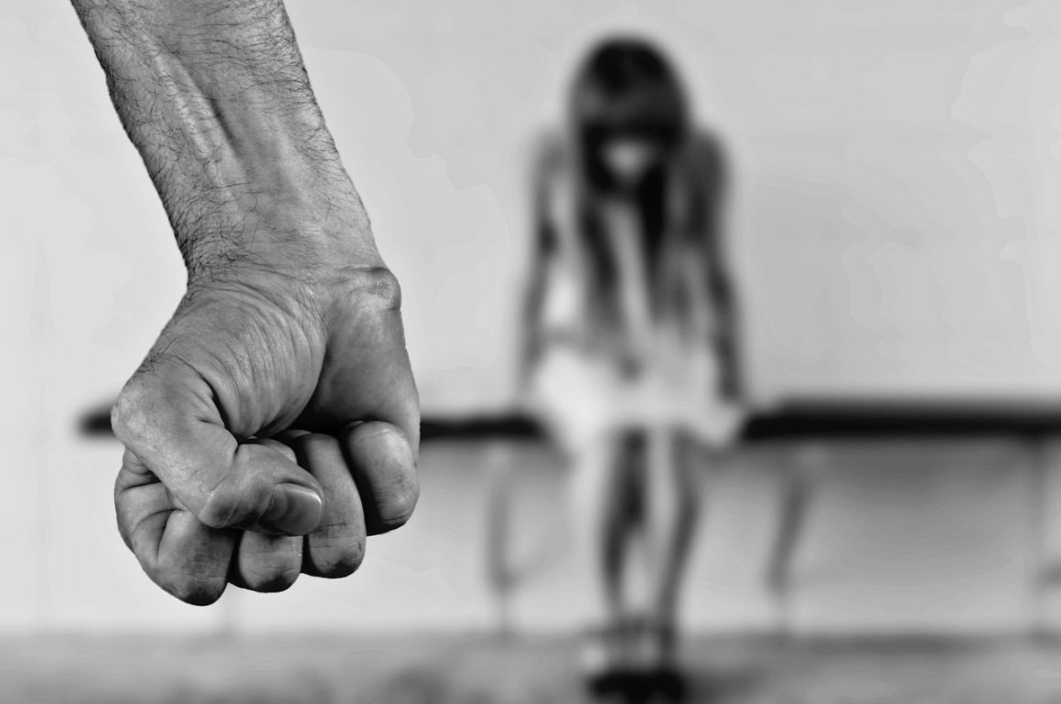 photo characterizing abuse - man's fist in foreground - woman bowing head in background