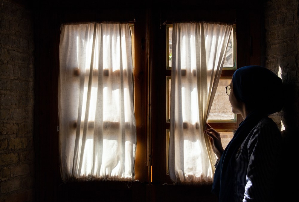 woman peeking outside past window curtain