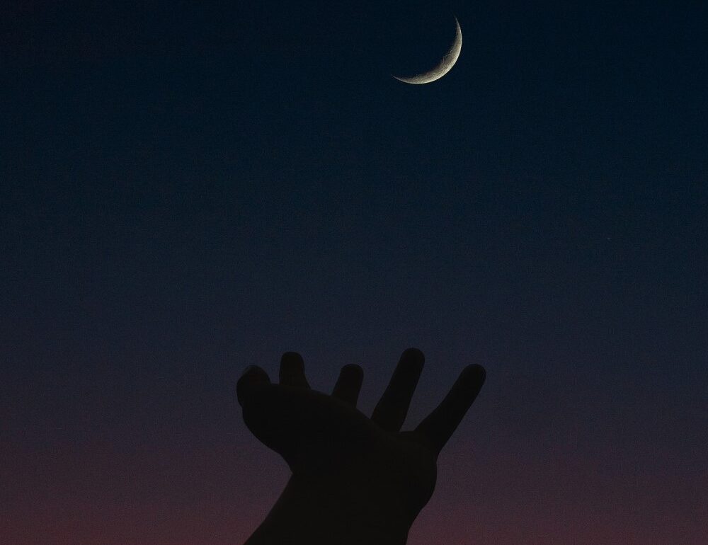 hand reaching up toward crescent moon