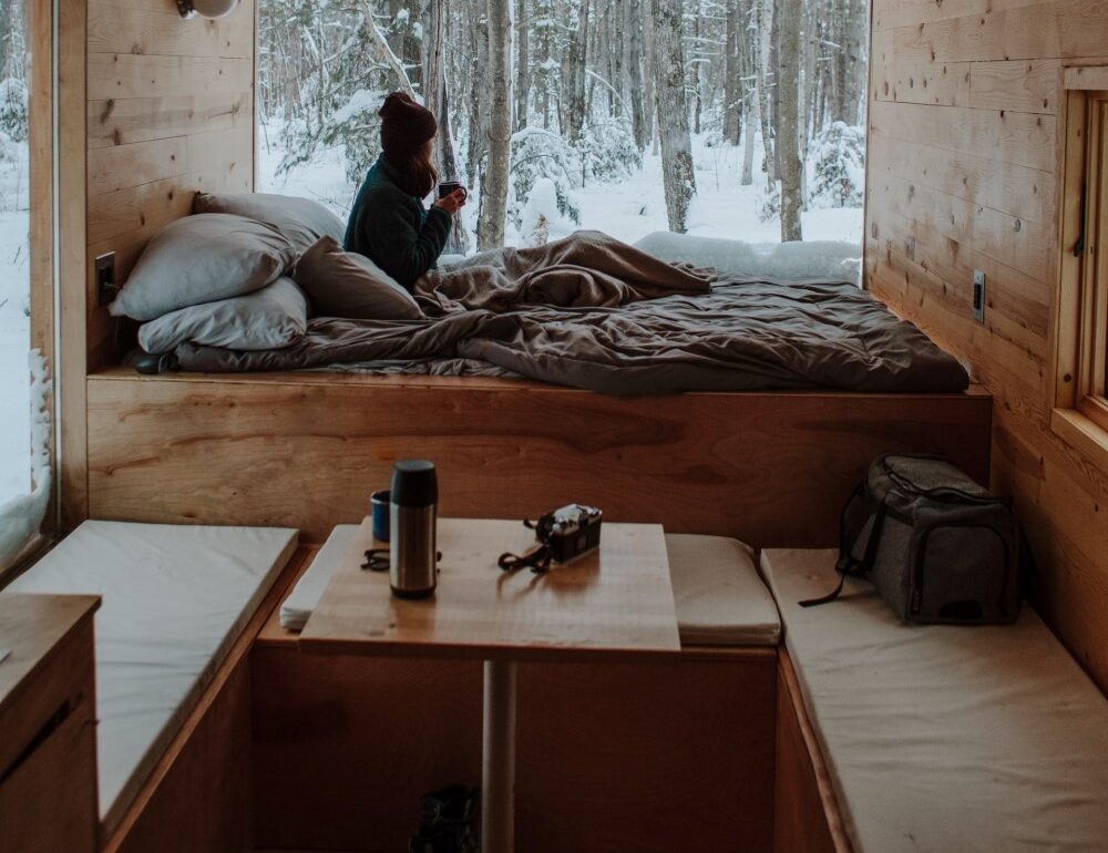 small room in winter as woman drinks hot beverage on a bed in a tiny house