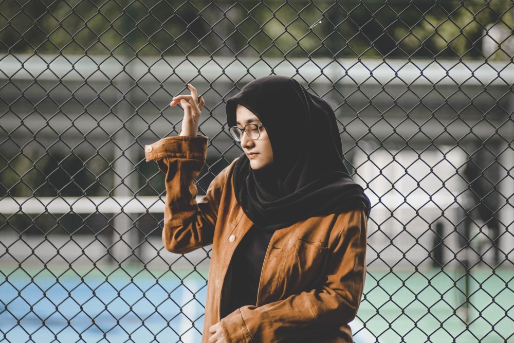 woman in black hijab scarf by chain link to tennis court