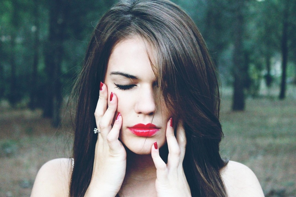 woman in forest with red lipstick and red nails holding her face in pain
