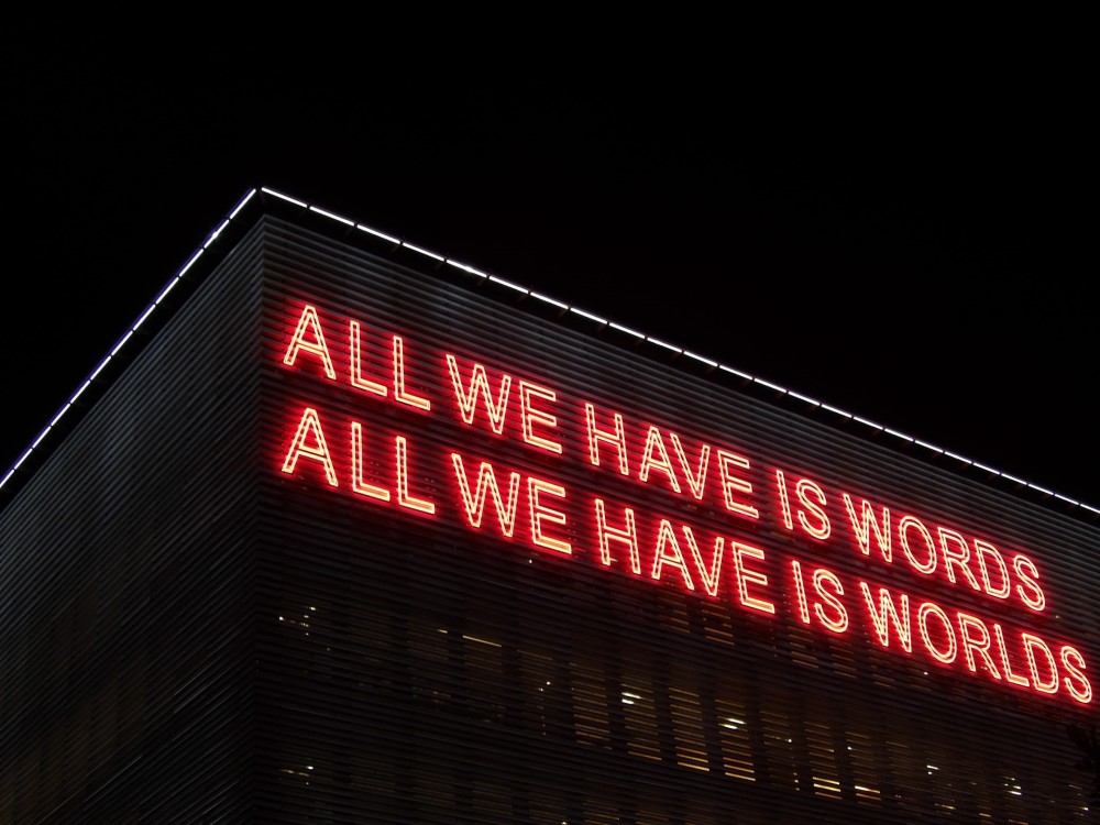 Neon sign that says ALL WE HAVE IS WORDS ALL WE HAVE IS WORLDS