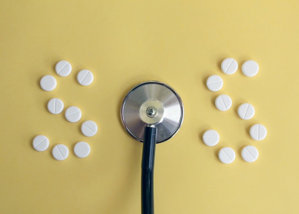 SOS spelled out by round white tablet pills and a stethoscope