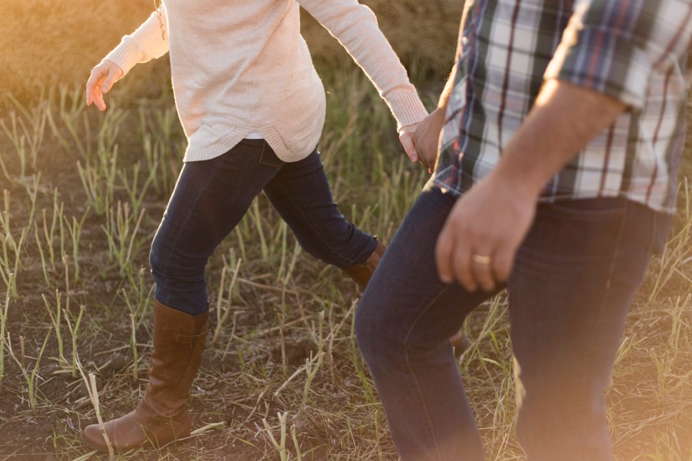 woman and man holding hands and walking through field