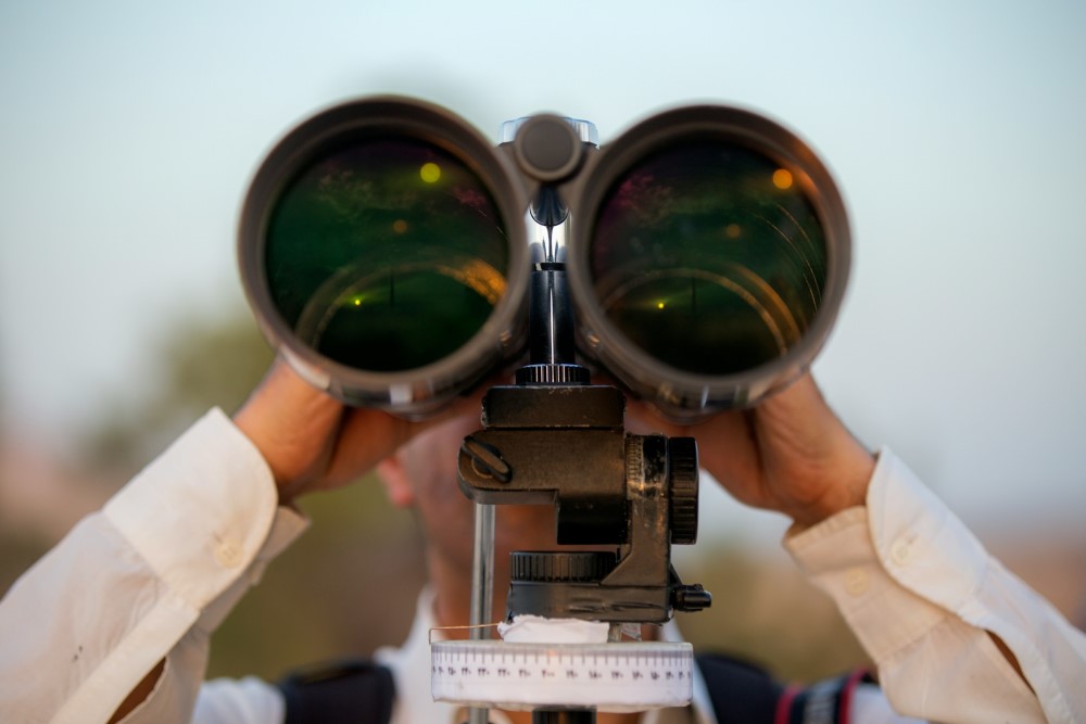 man in white shirt looking through large binoculars