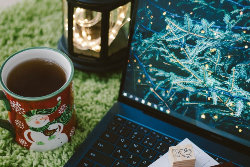 snowman mug next to laptop showing lights on Christmas tree